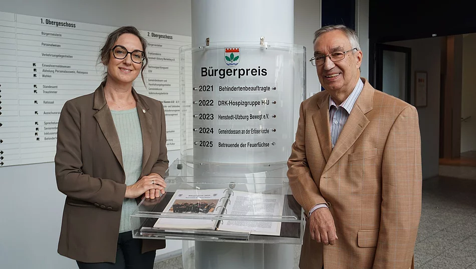 Bürgermeisterin Ulrike Schmidt und Bürgervorsteher Henry Danielski stehen vor der Säule mit den bisherigen Bürgerpreisträgerinnen und Bürgerpreisträgern.