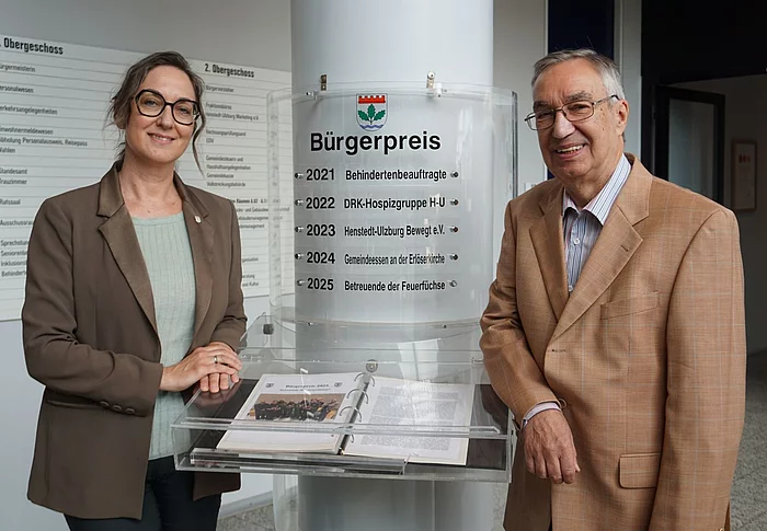 Bürgermeisterin Ulrike Schmidt und Bürgervorsteher Henry Danielski stehen vor der Säule mit den bisherigen Bürgerpreisträgerinnen und Bürgerpreisträgern.