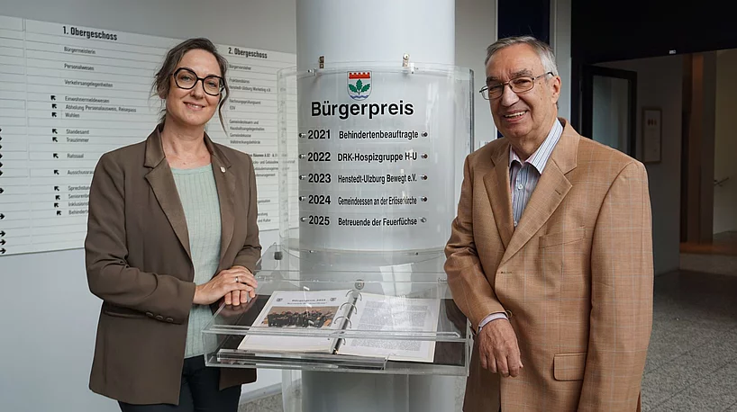 Bürgermeisterin Ulrike Schmidt und Bürgervorsteher Henry Danielski stehen vor der Säule mit den bisherigen Bürgerpreisträgerinnen und Bürgerpreisträgern.