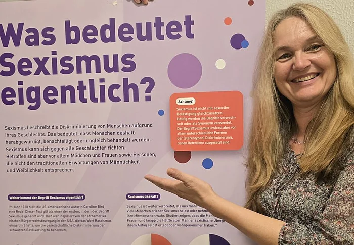 Eine Frau deutet auf ein Ausstellungsplakat.