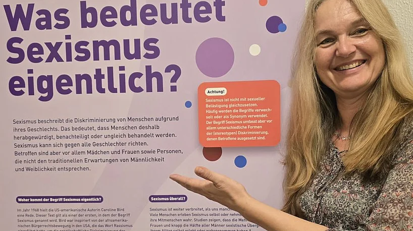 Eine Frau deutet auf ein Ausstellungsplakat.