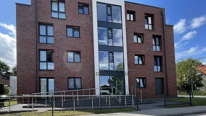 Barrierefreier Zugang zum Gebäudeeingang über eine leicht ansteigende Rampe mit Handläufen.