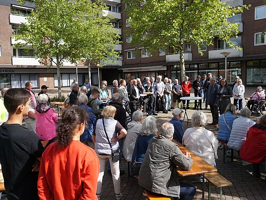 Zahlreiche Anwohnende und am Projekt Beteiligte stehen auf dem Markplatz uns hören sich eine Rede zur Eröffnung der sanierten Straße an.