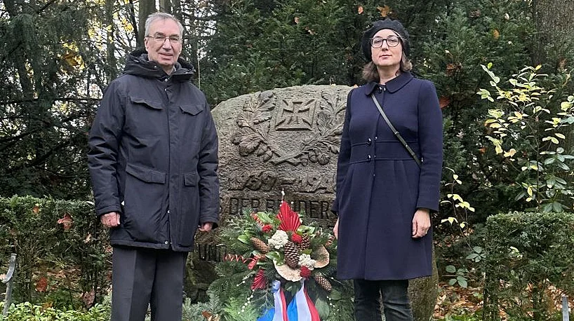 Zwei Personen stehen neben einem Kranz vor dem Ehrenmal.