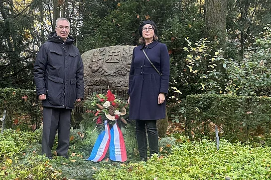 Zwei Personen stehen neben einem Kranz vor dem Ehrenmal.
