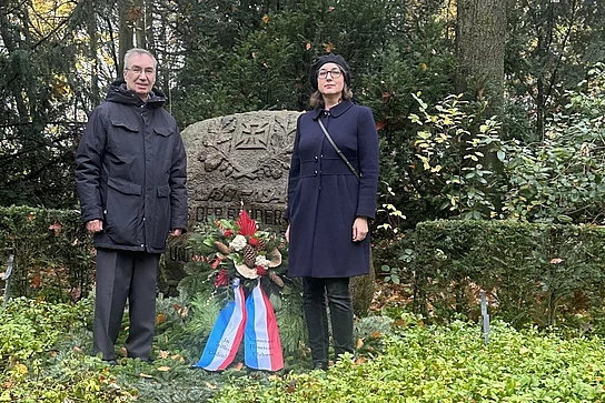 Zwei Personen stehen neben einem Kranz vor dem Ehrenmal.