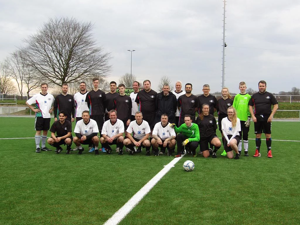 Die beiden Teams stehen für eine Gruppenfoto zusammen. Eine Reihe steht, eine Reihe sitzt davor.
