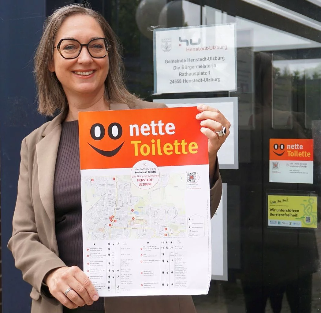 Bürgermeisterin Ulrike Schmidt präsentiert ein Plakat zur Aktion "Nette Toilette" vor dem Eingang des Rathauses.