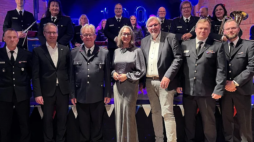 Sieben Personen stehen vor der Bühne, auf der der Feuerwehrmusikzug ist.