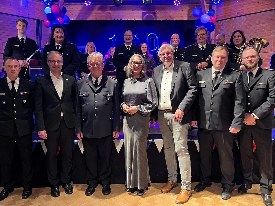 Sieben Personen stehen vor der Bühne, auf der der Feuerwehrmusikzug ist.