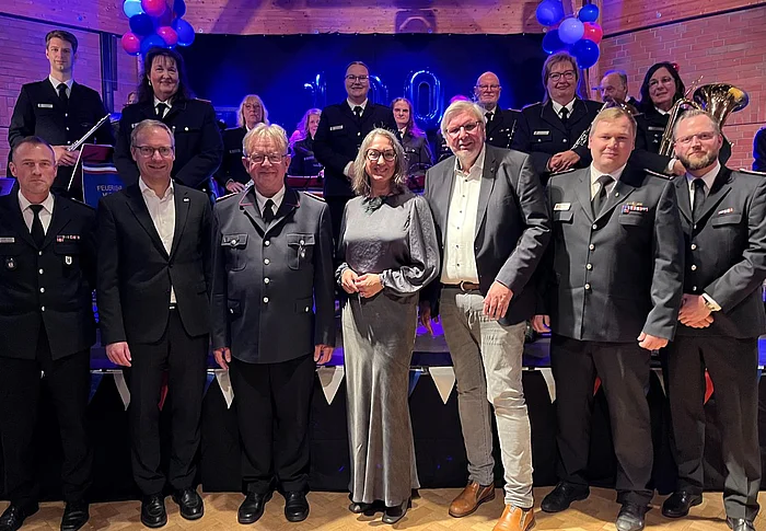 Sieben Personen stehen vor der Bühne, auf der der Feuerwehrmusikzug ist.