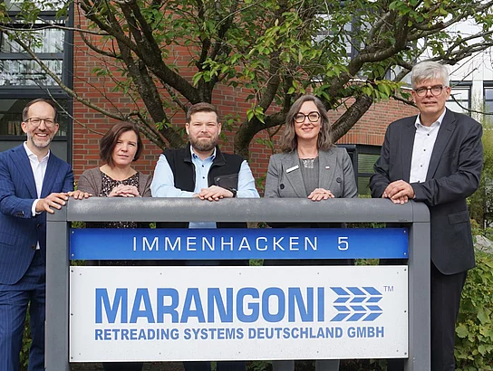 Fünf Personen stehen hinter einem Schild mit dem Firmenlogo.