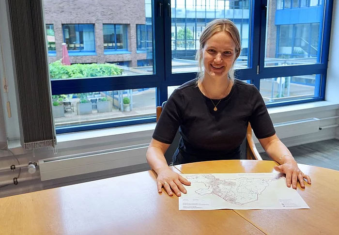 Klimaschutzmanagerin Hannah Grünewald sitz an einem Tisch im Rathaus und lächelt in die Kamera. Vor ihr liegt der Plan zur kommunalen Wärmeplanung.